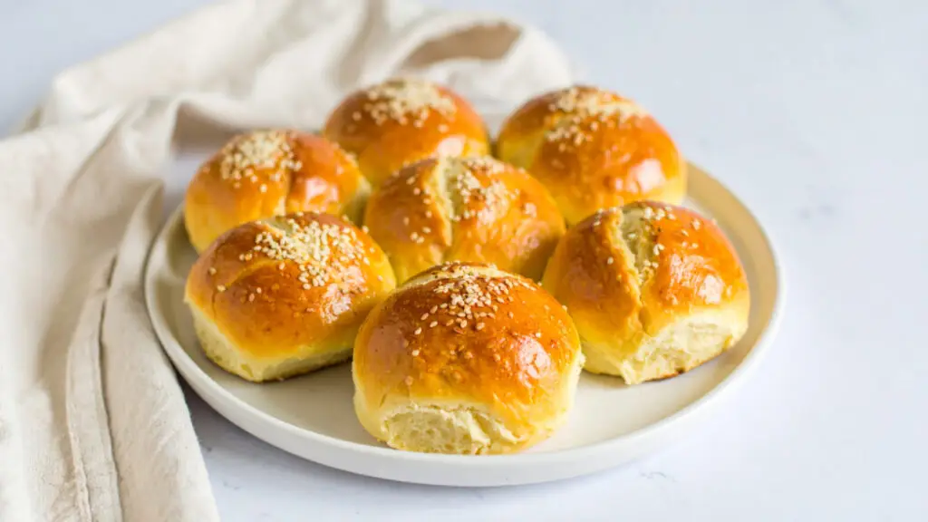 Fluffy golden cloud bread rolls topped with sesame seeds on a white plate